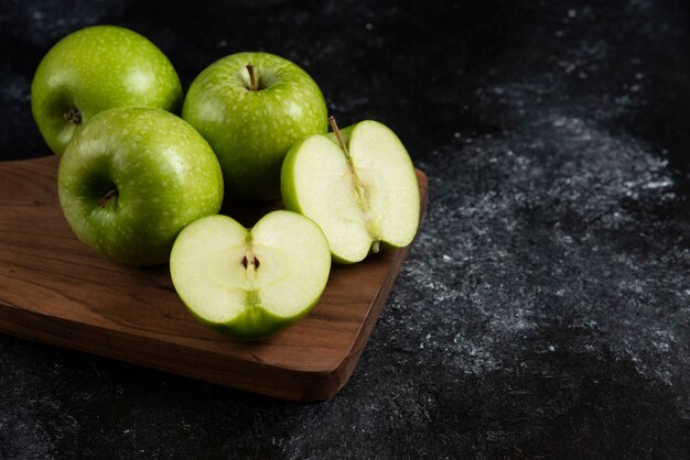 Pommes vertes mûres entières et tranchées sur planche de bois.