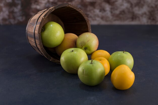 Pommes vertes et oranges dans un seau en bois