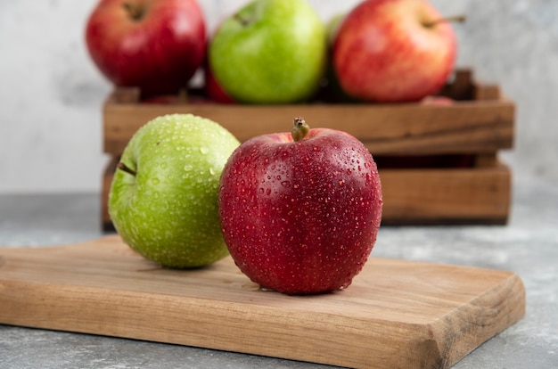 Pommes vertes et rouges entières humides sur une planche à découper en bois.