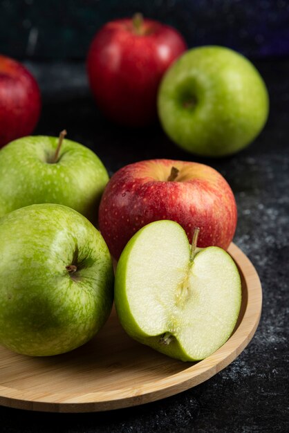 Pommes vertes et rouges entières et tranchées sur plaque de bois.