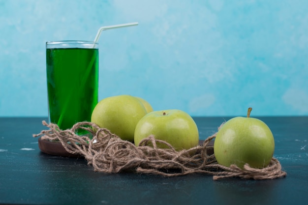 Pommes vertes avec un verre de jus sur une planche de bois.