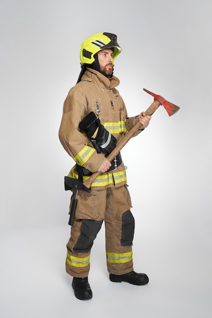 Photo gratuite un pompier barbu sérieux en pleine tenue tenant une hache rouge pour la lutte contre les incendies vue latérale d'un homme concentré