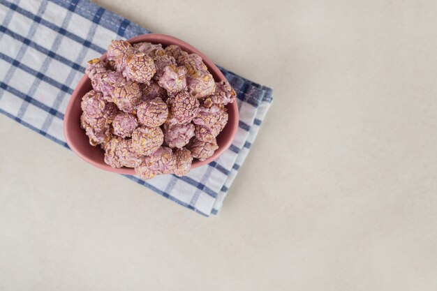 Pop-corn aromatisé violet dans un petit bol sur une serviette soigneusement pliée sur du marbre.