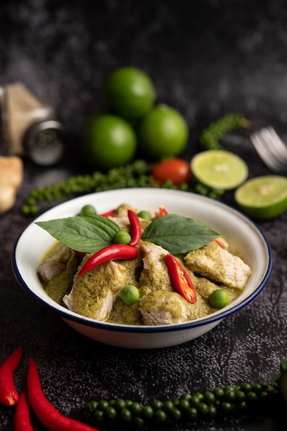 Porc au curry vert dans un bol blanc avec des épices sur un fond de ciment noir