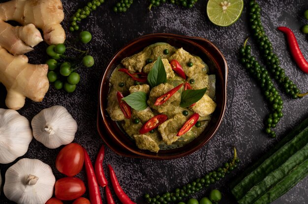 Porc au curry vert dans un bol brun avec des épices sur un fond de ciment noir