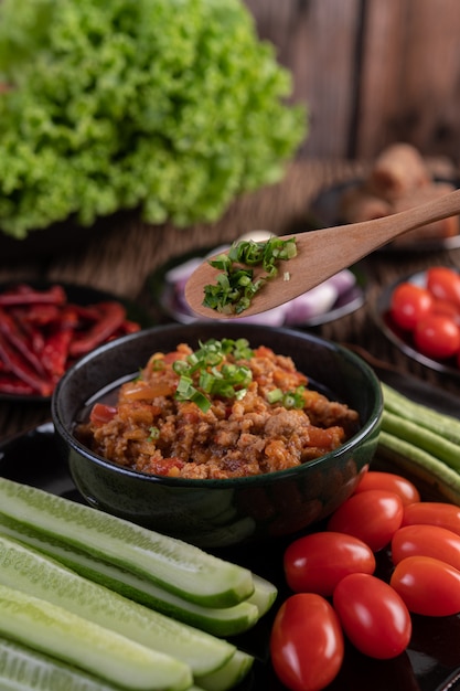 Porc doux dans un bol noir, avec concombres, haricots longs, tomates et accompagnements