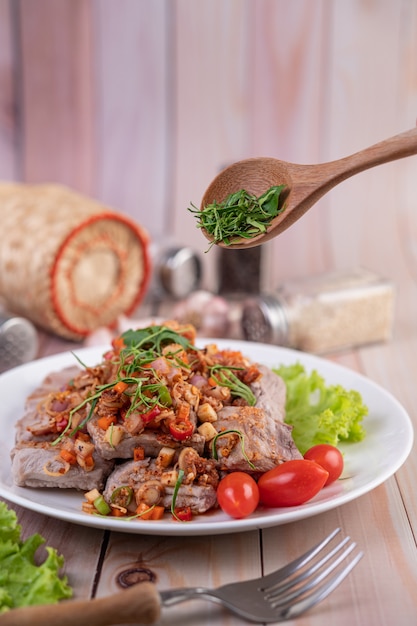 Porc épicé haché avec des tomates et de la laitue sur une plaque blanche sur une table en bois.