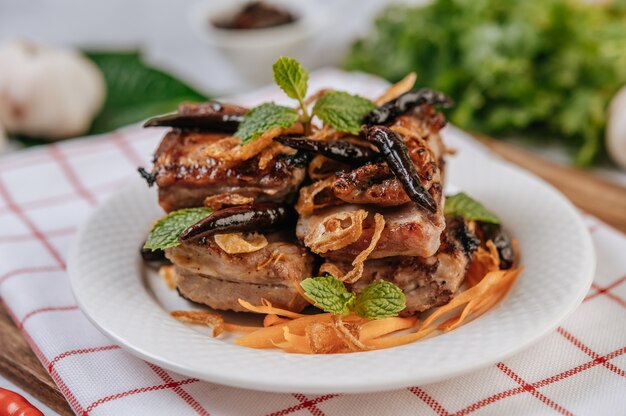 Porc Frit avec Chili Frit Oignon frit et menthe dans une assiette blanche.