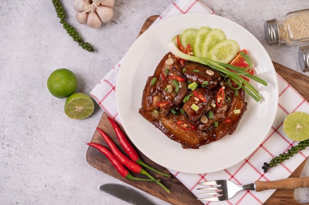 Porc sucré sur une assiette blanche avec oignons verts hachés, piment, citron vert, concombre, tomate et ail.