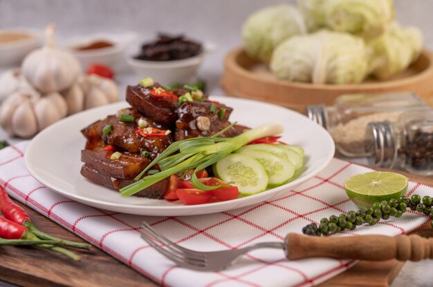 Porc sucré sur une assiette blanche avec oignons verts hachés, piment, citron vert, concombre, tomate et ail.