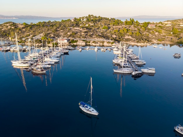 Port de la mer Égée avec plusieurs yachts amarrés près de quais, verdure, eau bleue, vue depuis le drone, Grèce