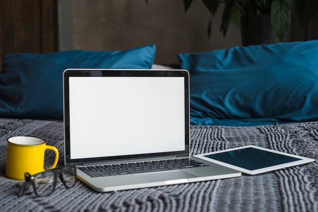 Portable; tablette numérique; lunettes et tasse sur le lit