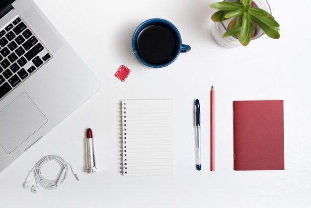 Portable; tasse de thé; écouteur; rouge à lèvres et papeterie de bureau sur le bureau blanc