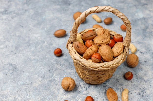 Portée du panier dans divers types de noix en coques, arachides, amandes, noisettes et noix sur une surface en béton