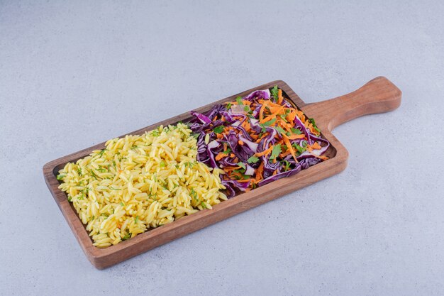 Portions de riz brun et salade de chou rouge dans un bac sur fond de marbre.