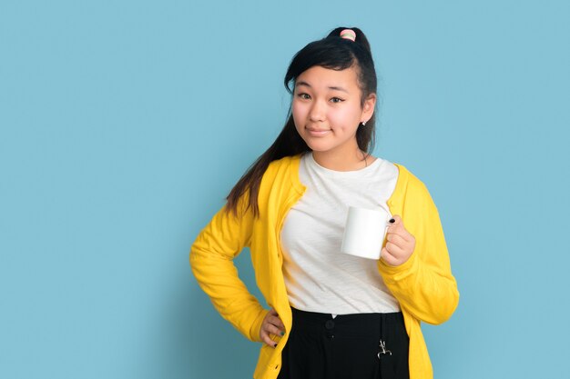 Portrait D'adolescent Asiatique Isolé Sur Fond Bleu Studio. Beau Modèle Femme Brune Aux Cheveux Longs. Concept D'émotions Humaines, Expression Faciale, Ventes, Publicité. Boire Du Café Ou Du Thé.