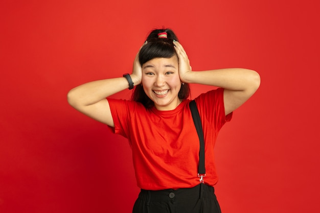 Portrait d'adolescent asiatique isolé sur fond de studio rouge. Beau modèle femme brune aux cheveux longs en casual. Concept d'émotions humaines, expression faciale, ventes, publicité. Étonné, choqué.