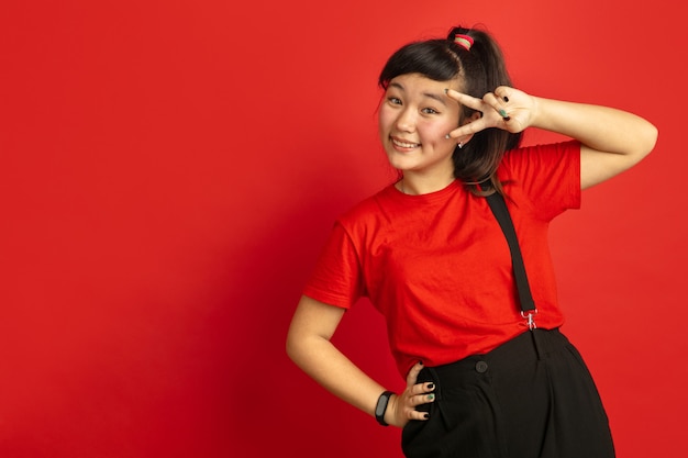 Portrait d'adolescent asiatique isolé sur fond de studio rouge. Beau modèle femme brune aux cheveux longs dans un style décontracté. Concept d'émotions humaines, expression faciale, ventes, publicité. Posant mignon.