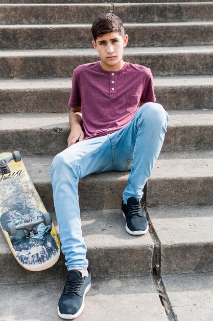 Portrait d&#39;un adolescent assis sur un escalier en béton avec skateboard