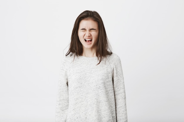 Portrait d'un adolescent enfantin qui est sur le point de pleurer, debout les yeux fermés et hurlant à haute voix.