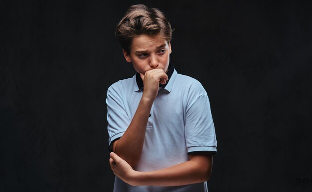 Portrait d'un adolescent pensif vêtu d'un t-shirt blanc. Isolé sur le fond sombre.