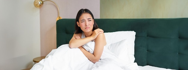 Photo gratuite portrait d'une adolescente asiatique allongée dans son lit et grimaçant ne voulant pas se réveiller en regardant par la fenêtre