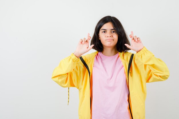 Portrait d'une adolescente en gardant les doigts croisés dans un t-shirt, une veste et une vue de face confiante