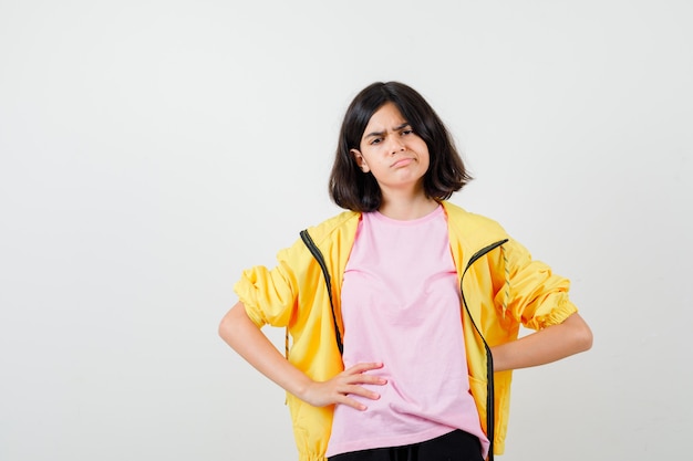 Portrait d'une adolescente gardant la main derrière le dos tout en posant en t-shirt, veste et regardant triste vue de face
