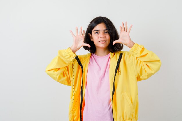 Portrait d'une adolescente montrant un geste d'abandon en t-shirt, une veste jaune et à la vue de face perplexe