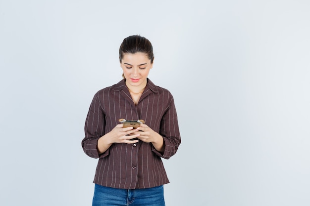 Portrait d'une adolescente utilisant un smartphone en chemise rayée marron et regardant la vue de face occupée