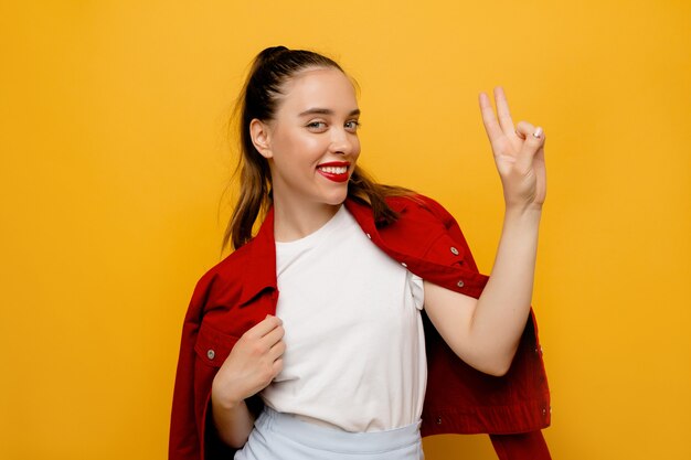 Portrait d'adorable fille charmante debout avec signe de paix sur jaune