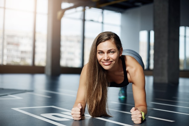 Portrait d'adulte belle femme faisant des exercices de planche de coude sur un sol de gym. Concept de corps de remise en forme saine.