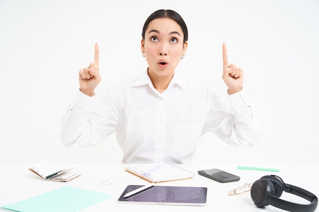 Photo gratuite portrait d'affaires et de profession d'une femme asiatique sur le lieu de travail est assis au bureau et pointe vers le haut montre bann