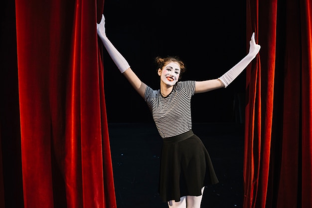 Portrait d&#39;un artiste mime féminin heureux tenant un rideau rouge