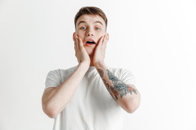 Portrait avant demi-longueur mâle attrayant sur fond de studio gris. Jeune homme surpris émotionnel debout avec la bouche ouverte. Émotions humaines, concept d'expression faciale