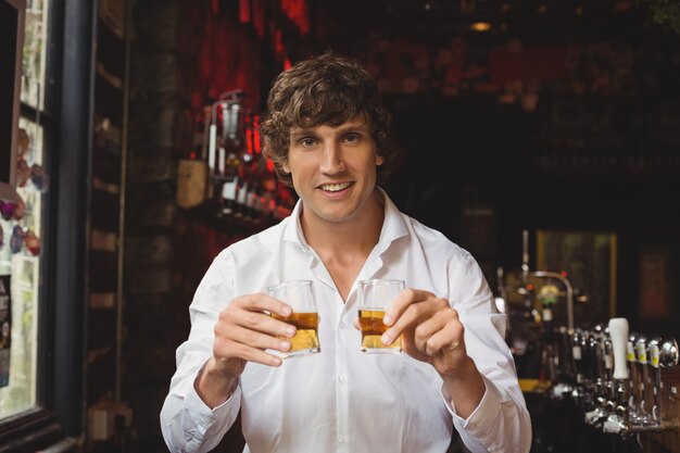 Portrait de barman tenant des verres à whisky au comptoir du bar