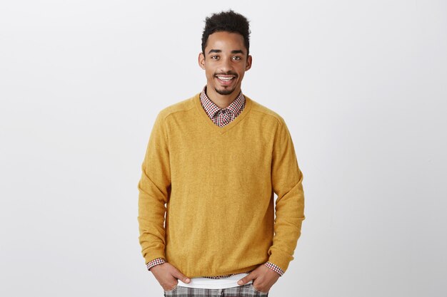 Portrait de beau afro-américain avec une coiffure afro en pull jaune élégant tenant la main dans les poches, souriant avec désinvolture
