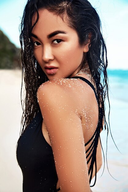 portrait, de, beau, caucasien, bains de soleil, modèle femme, à, longs cheveux noirs, dans, maillot de bain sombre, poser, sur, plage été, à, sable blanc, sur, ciel bleu, et, mur océan