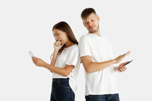 Portrait de beau jeune couple isolé. Expression faciale, émotions humaines. Homme et femme tenant des smartphones et ont peur de son écran.