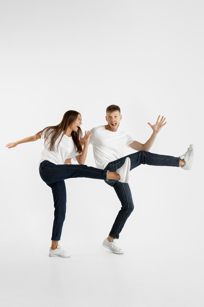 Portrait de beau jeune couple isolé sur fond de studio blanc. Expression faciale, émotions humaines, concept publicitaire. Copyspace. Femme et homme sautant, dansant ou courant ensemble.