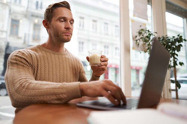 Photo gratuite portrait d'un beau jeune homme assis dans un café avec un ordinateur portable nomade numérique indépendant travaillant à l'extérieur