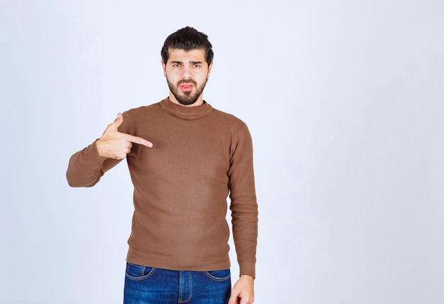 Portrait de beau jeune homme barbu en pull marron debout et se pointant. photo de haute qualité