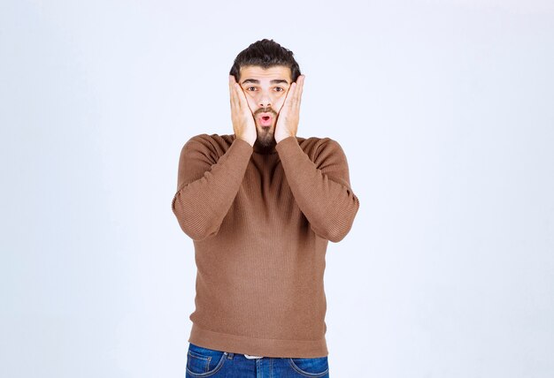 Portrait d'un beau jeune homme en pull décontracté tenant les paumes près des joues.