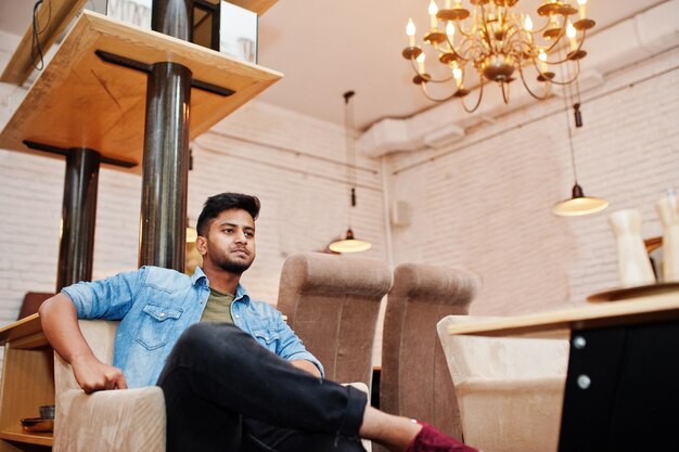 Portrait d'un beau jeune indépendant indien sud-asiatique barbu réussi en chemise de jeans bleu assis dans un café et se reposer