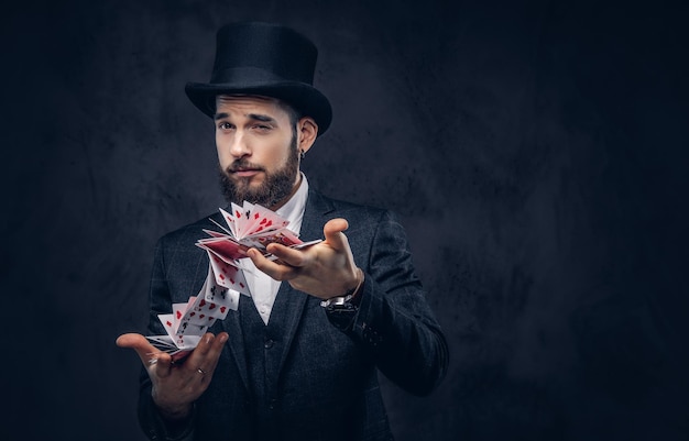 Photo gratuite portrait d'un beau magicien en costume noir, montrant un tour avec des cartes à jouer sur fond sombre.