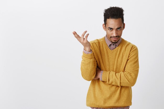 Portrait de beau mâle agacé avec coupe de cheveux afro dans des vêtements jaunes, faisant des gestes, exprimant la confusion, fronçant les sourcils, mécontent et interrogé lors de l'accusation