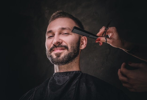 Portrait d'un beau mâle dans un salon de coiffure d'élite, il reçoit des soins capillaires de la part d'une femme.