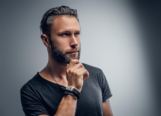 Portrait de beau mâle macho vêtu d'un t-shirt gris isolé sur fond gris.