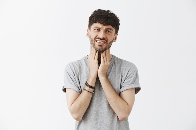 Portrait de beau mec en colère posant contre le mur blanc