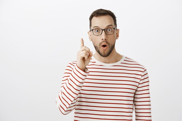 Portrait de beau mec excité à lunettes noires, ayant l'idée et levant l'index en geste eureka